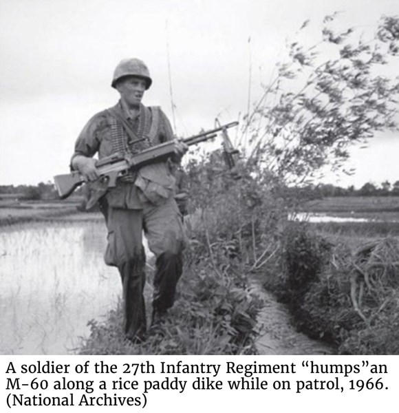 A soldier of the 27th Infantry Regiment “humps” an M-60 along a rice paddy dike while on patrol, 1966. (National Archives) 